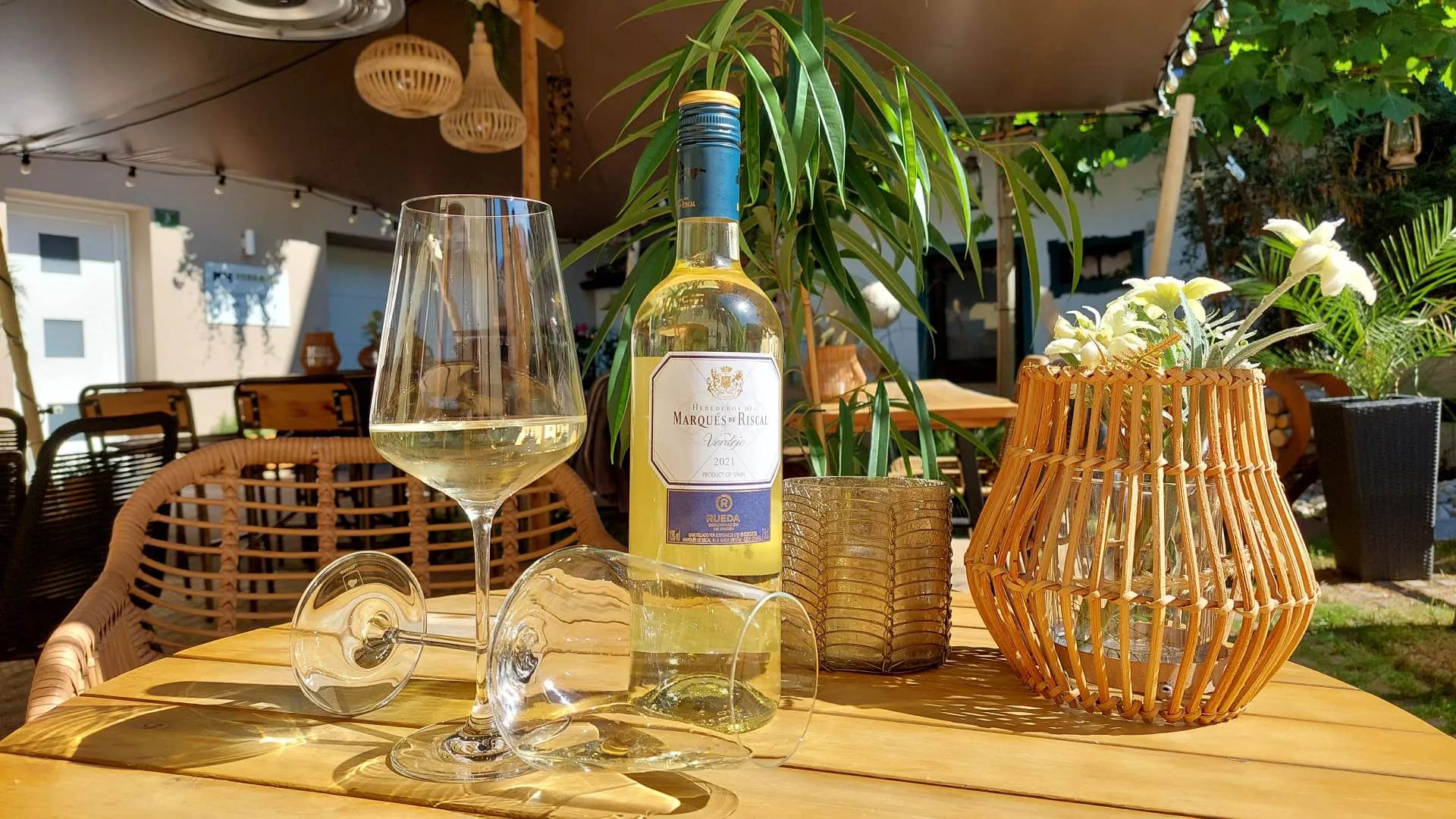 Weinglas, Flasche Weißwein und Pflanzen auf einem Tisch im Freien.