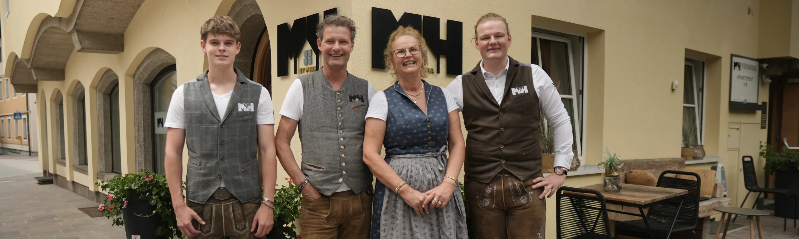 Familie vor einem Restaurant mit Pflanzen und Tischen.